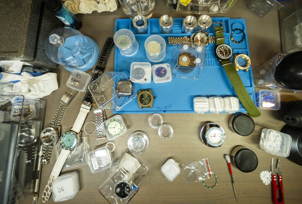 Watch parts laid out on a blue bench mat: dial blanks, bezel inserts, bracelets and a turquoise dial.